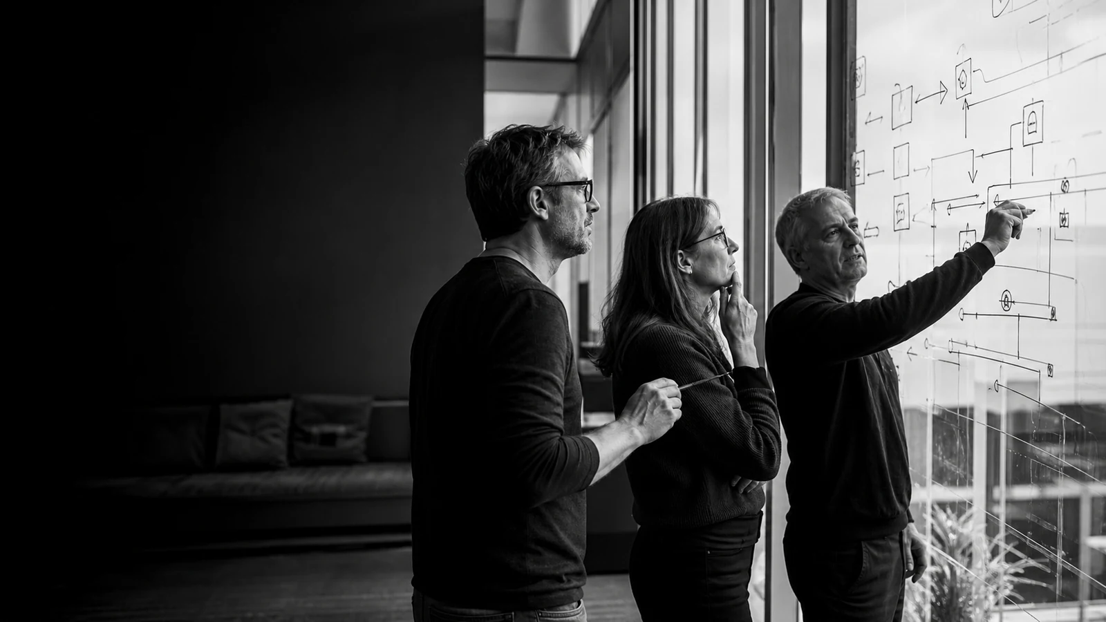 Three people mapping a complex workflow together on a glass wall