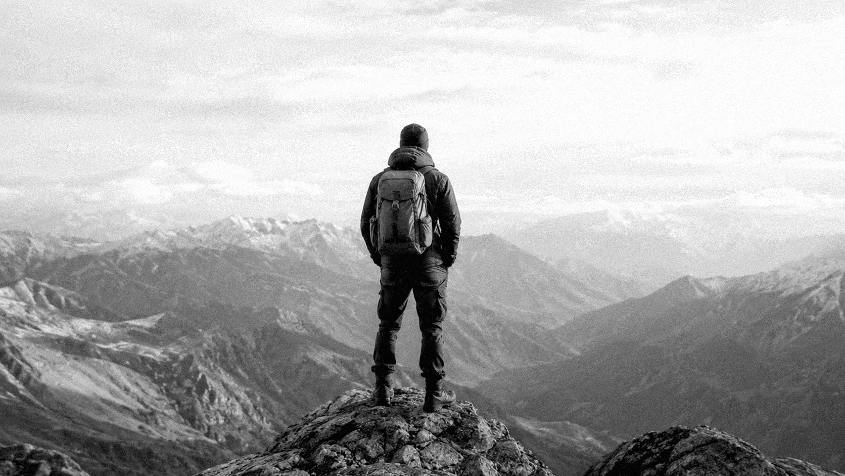 A lone hiker standing on a summit, looking out over a mountain range